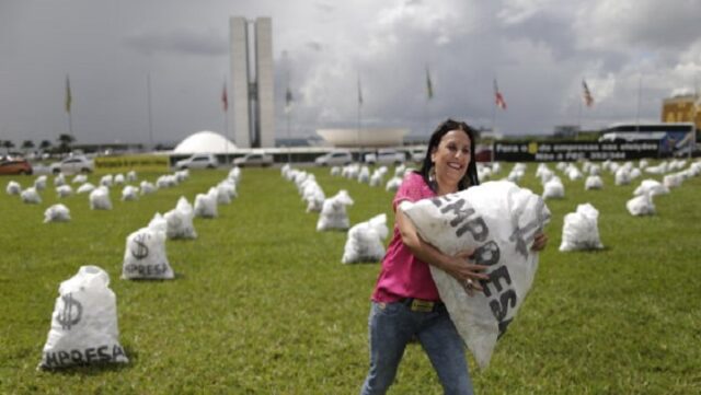 A woman carries a replica of a bag full of money in front of the National Congress during a protest symbolizing the donations of private companies for election campaigns, in Brasilia